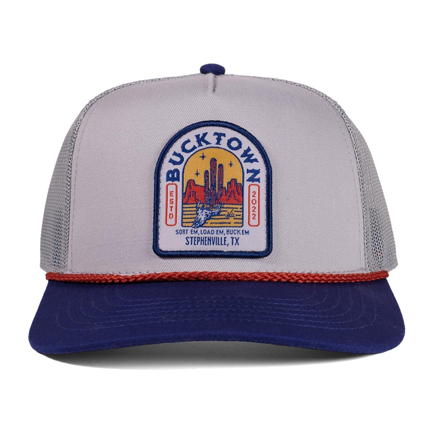 A gray and navy Sundown Hat by Rural Cloth features a red brim braid, "Bucktown" and "Stephenville, TX" front patch with desert scene, plus classic western snapback style and "Sort 'Em, Load 'Em, Buck 'Em.