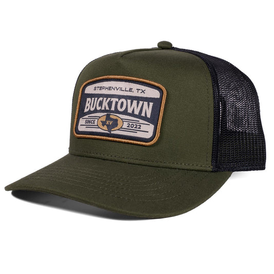 The Bucktown Outrider Hat by Rural Cloth features an olive green and black mesh design with a "Stephenville, TX Bucktown Since 2022" patch, a curved bill, and a structured crown—perfect for fans of Bucktown.