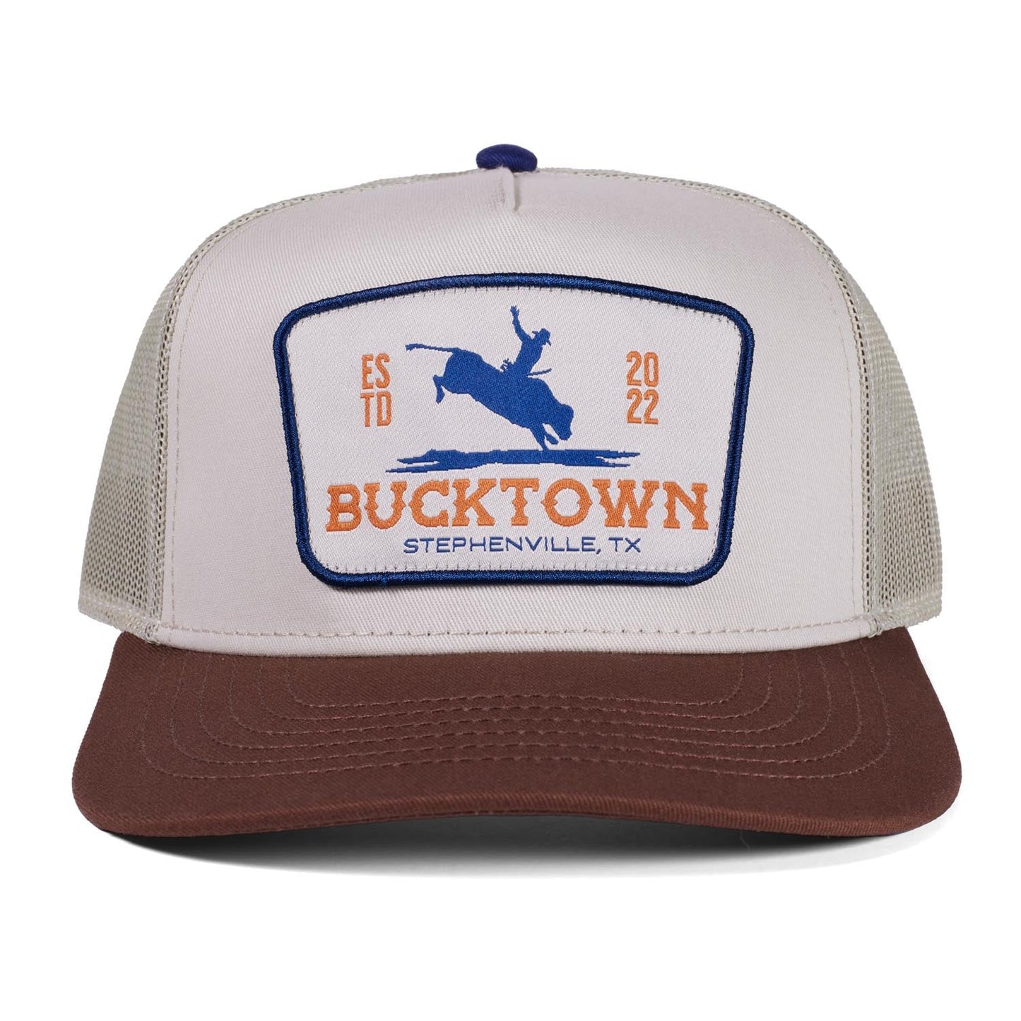 The Rural Cloth Last Out Hat is a two-tone western snapback with a white front, brown bill, and a patch reading "Bucktown Stephenville, TX" plus a bucking horse, "ESTD 2022," and Bucktown XV Ranch in orange and blue.
