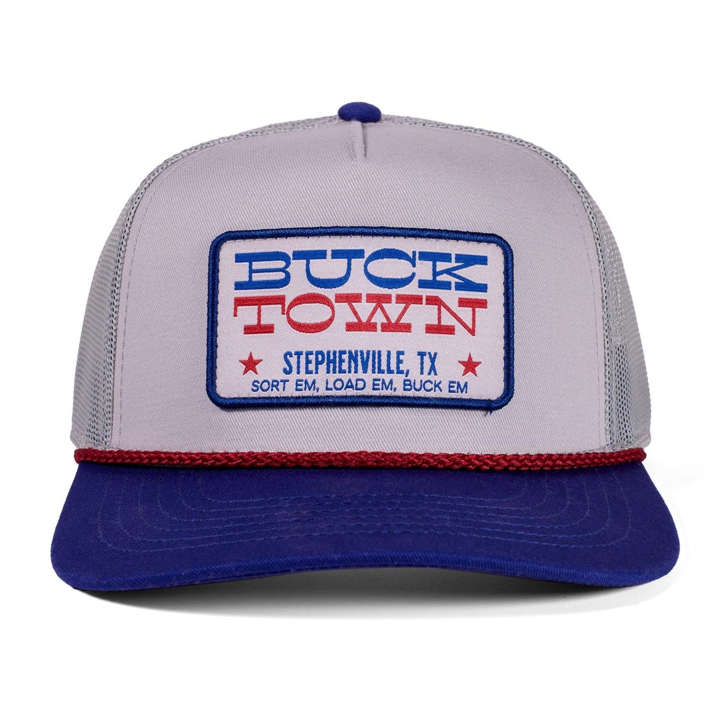 The Rural Cloth Patriot Hat is a gray and blue trucker hat with a red rope, featuring a "Buck Town" patch in blue and red. Below it reads "Stephenville, TX, Sort Em, Load Em, Buck Em" in red for an Americana look.