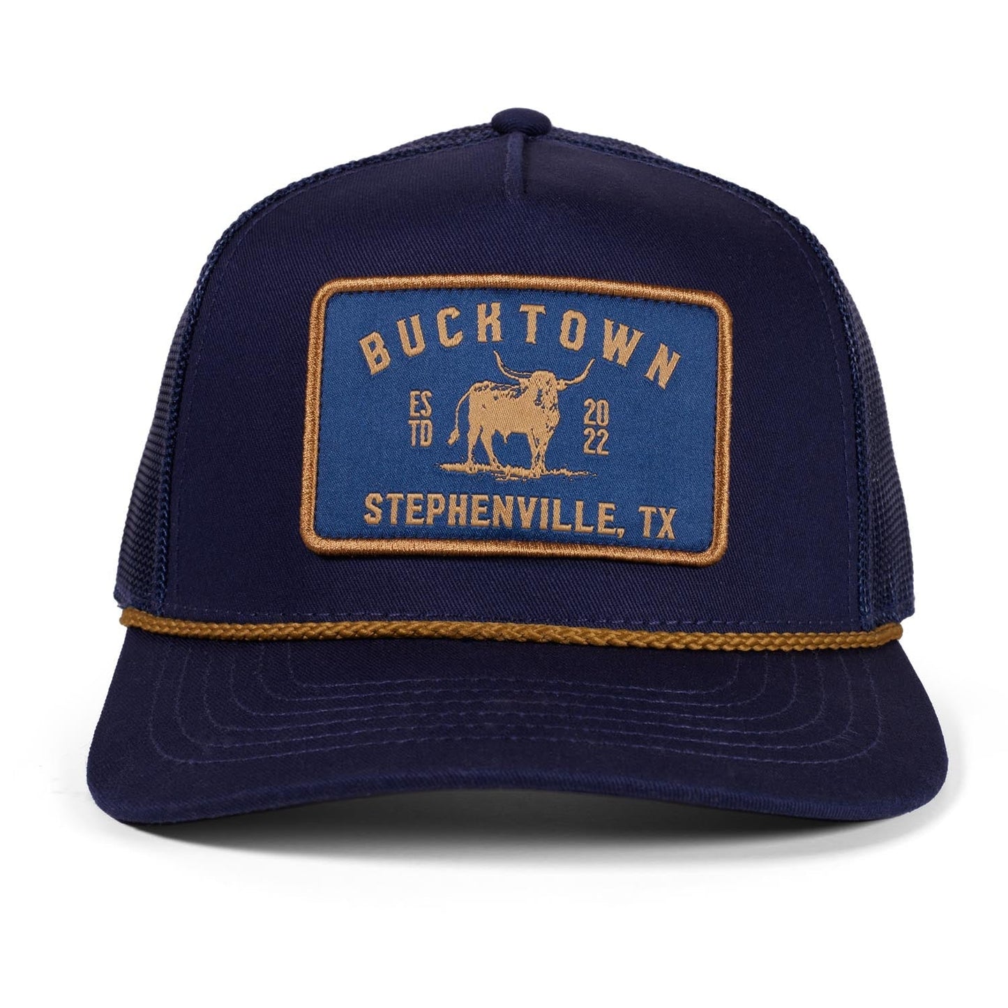 The Rural Cloth Stockman Hat is a navy blue trucker with a yellow "BUCKTOWN, ESTD 2022, STEPHENVILLE, TX" patch and bucking bull graphic. It features an adjustable snapback and a decorative yellow braided visor rope.