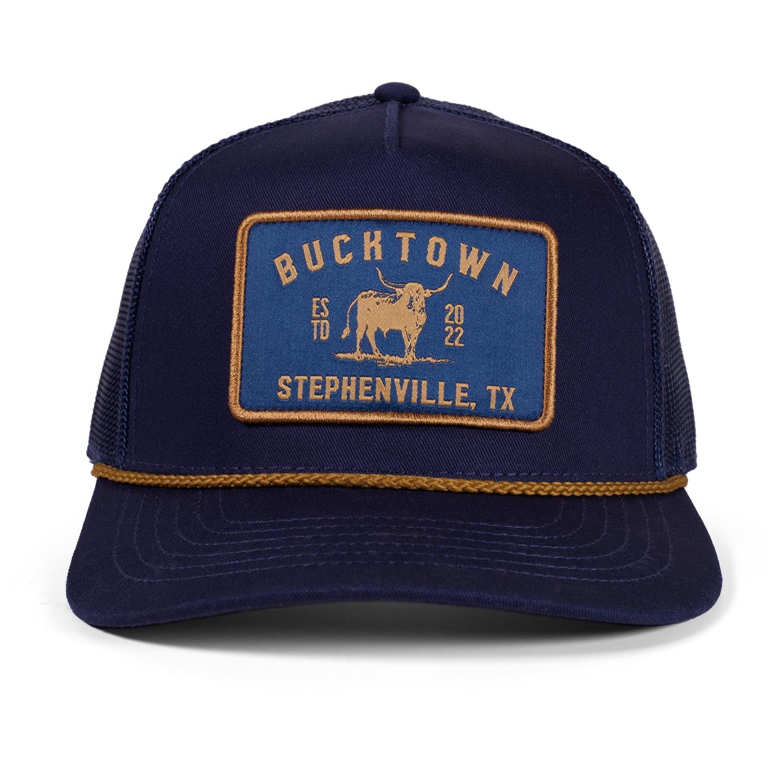 The Rural Cloth Stockman Hat is a navy blue trucker with a yellow "BUCKTOWN, ESTD 2022, STEPHENVILLE, TX" patch and bucking bull graphic. It features an adjustable snapback and a decorative yellow braided visor rope.